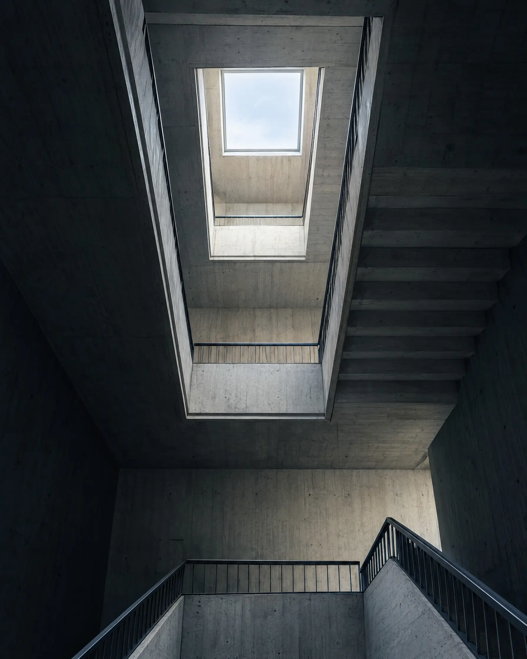 Une cage d’escalier en béton apparent vue d’en bas vers la verrière